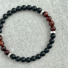 a bracelet with black, red and white beads sits on a gray surface in front of a grey background