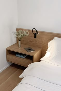 a bed with white sheets and a wooden night stand next to it on top of a hard wood floor