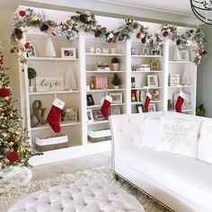 a living room decorated for christmas with white furniture and red stockings on the fireplace mantel