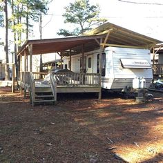 an rv is parked in the woods next to a house with a porch and awning