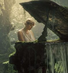 a woman standing in front of a fountain with moss growing on it's sides