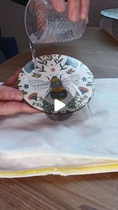 a person pouring water into a plate on top of a wooden table next to a napkin