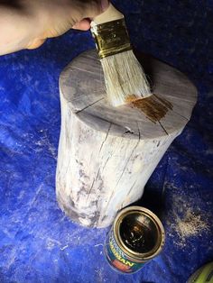 a person holding a paint brush on top of a piece of wood next to cans