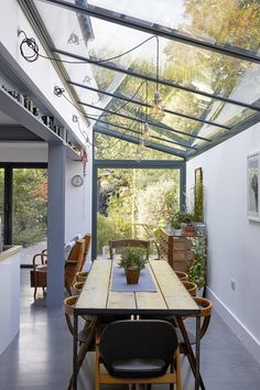 a table and chairs in a room with a glass roof over the dining area is surrounded by potted plants