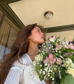 a woman holding a bouquet of flowers in her hand and looking up into the sky