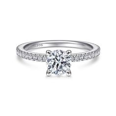 a white gold engagement ring with diamonds on the band and a round brilliant cut diamond center