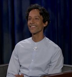 a smiling man sitting in front of a blue curtain