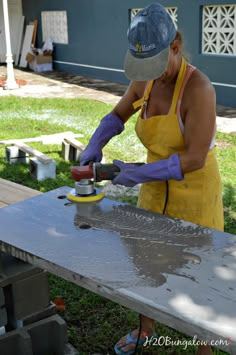 a woman in yellow apron and hat sanding concrete