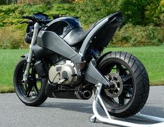 a black motorcycle parked on the street next to some grass and trees in the background