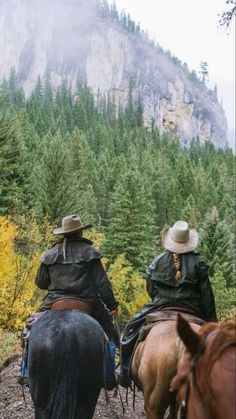 two men riding horses on a trail in the mountains with trees and rocks behind them