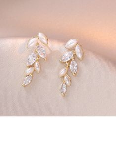 two pairs of gold tone earrings with white stones and leaves on the front, set against a light pink background