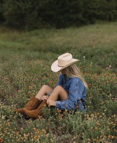 a woman wearing a cowboy hat sitting in a field