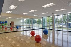 an empty gym with exercise balls on the floor and large windows in the back ground