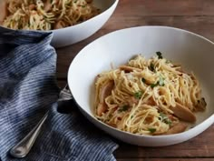 two white bowls filled with pasta on top of a wooden table