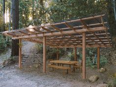 a picnic table under a wooden pergoline in the middle of a wooded area