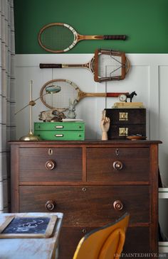 a dresser with tennis rackets on top of it next to a green painted wall