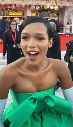 a woman in a green dress is smiling at the camera and people are standing behind her