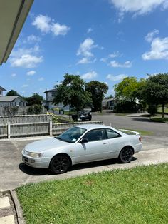 a white car parked on the side of a road next to a fence and grass