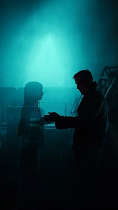 two people standing in the dark with their hands out to each other and lights behind them