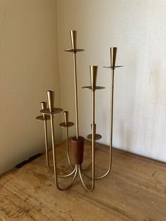 three brass candlesticks on a wooden table in front of a white wall and wood floor