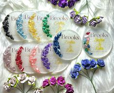 six flower brooches are shown on a white sheet with purple, blue, green, and yellow flowers