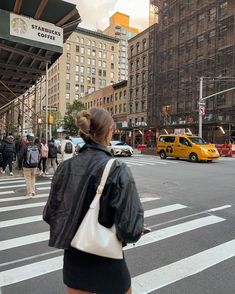 a woman walking across a cross walk in front of tall buildings with cars and people