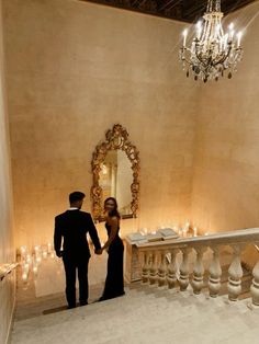 a man and woman standing in front of a chandelier with candles on it