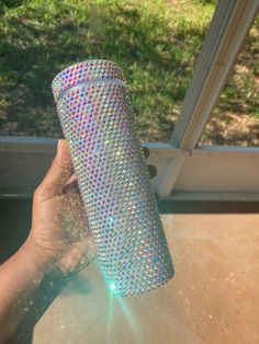 a person holding up a cup that is covered in sequins and has the sun shining through it