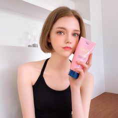 a woman holding up a tube of sunscreen in front of her face and looking at the camera