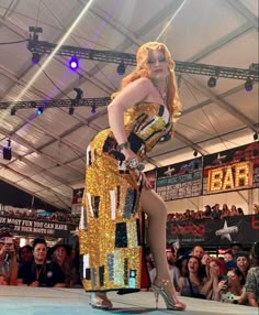 a woman in a gold and black outfit is on stage with people watching from the audience