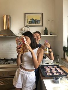 two people standing in a kitchen with doughnuts