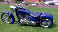 a blue motorcycle parked on top of a lush green field in front of a house