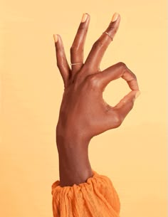 a woman's hand making the v sign with her fingers, against an orange background