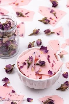 a white bowl filled with purple flowers next to a jar of pink petals on top of a table