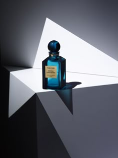 a bottle of blue perfume sitting on top of a white and black surface with the light coming through it