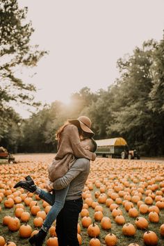 a man holding a woman in his arms while standing in a field full of pumpkins