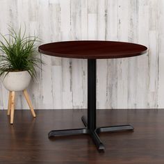 a small round table sitting next to a potted plant on a wooden floor in front of a white wall