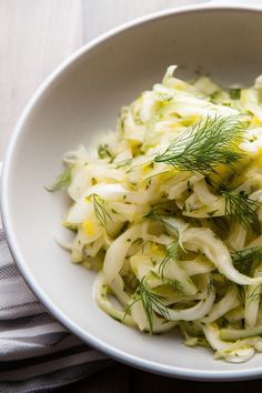 a white bowl filled with coleslaw on top of a wooden table next to a napkin