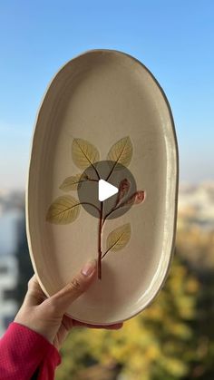 a person holding up a plate with a flower painted on the front and side of it