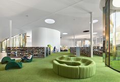 the interior of a public library with green carpeting and circular seating areas, bookshelves, and glass walls