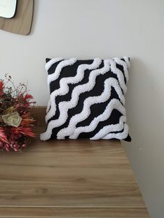 a black and white pillow sitting on top of a wooden table next to a vase with flowers