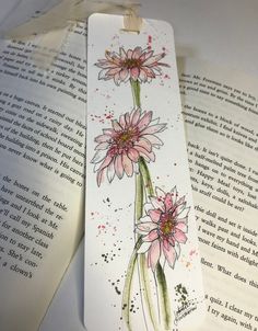 an open bookmark with pink flowers on it and watercolors in the background