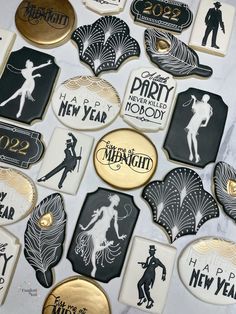 many decorated cookies are displayed on a white tablecloth with black and gold decorations, including new year's eve tags