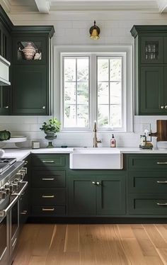 a kitchen with dark green cabinets and white counter tops is pictured in this image, there are two windows above the sink