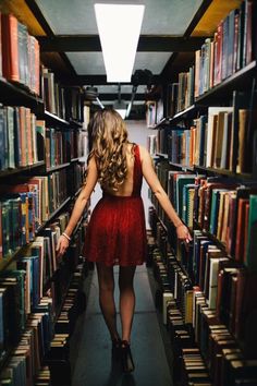 a woman in a red dress walking through a library filled with books