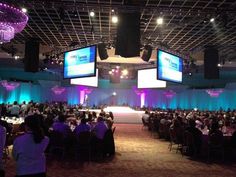 a room full of people sitting at tables with large screens on the wall above them