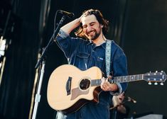 a man holding a guitar while standing on top of a stage next to a microphone