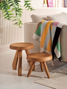 two wooden stools sitting next to each other on a white floor in front of a couch