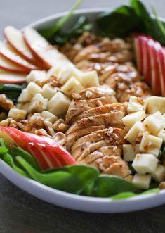 a white bowl filled with sliced apples, meat and veggies on top of it