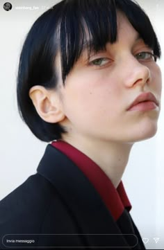 a woman with black hair wearing a suit and red tie looking off into the distance